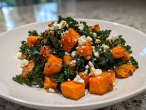 Close-up of a vibrant sweet potato salad featuring roasted orange sweet potato cubes, dark green kale, and crumbled white feta cheese.