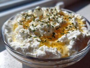 A close-up of creamy white whipped feta dip drizzled with golden honey and sprinkled with green herbs.