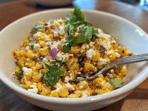 A close-up view of a vibrant street corn salad featuring charred corn kernels, crumbled white cheese, red onion, and cilantro.