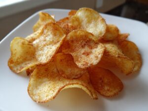 A close-up shot of a pile of golden, seasoned air fryer potato chips served on a white plate.