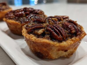 Close-up of a freshly baked mini pecan pie showing a flaky crust and glossy pecan topping.
