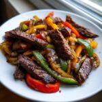 A close-up serving of amazing steak fajitas featuring seared strips of beef mixed with colorful sautéed bell peppers and onions.