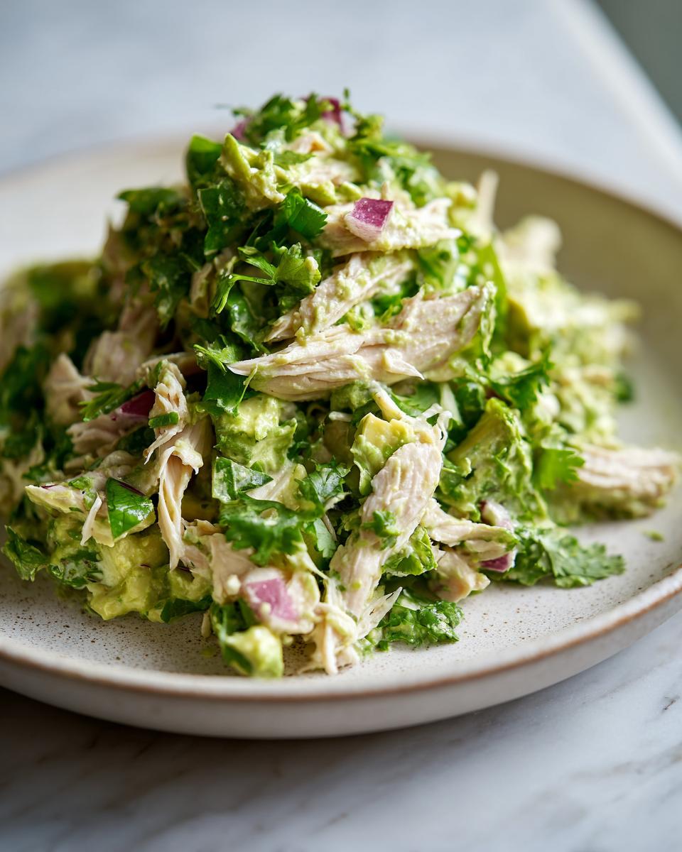 A close-up of a vibrant mound of avocado chicken salad mixed with chunks of avocado, red onion, and fresh cilantro.