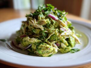 A vibrant mound of avocado chicken salad mixed with red onion and cilantro, served on a white plate.