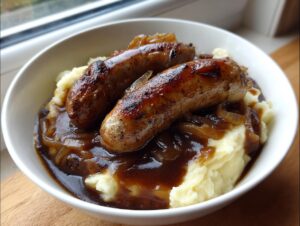 Two browned sausages served over creamy mashed potatoes and smothered in onion gravy, classic bangers and mash.
