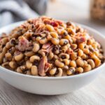A close-up of a white bowl filled with savory black eyed peas mixed with shredded ham.