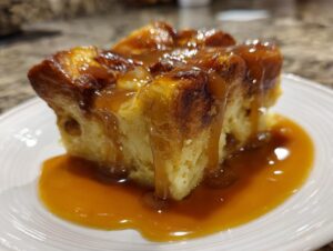 A close-up shot of a square slice of bread pudding with bourbon sauce generously drizzled over the top.