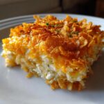 A close-up serving of cheesy potato casserole topped with melted cheddar and crispy cornflakes.