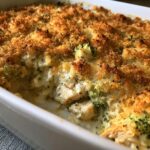 A close-up view of a creamy Chicken Divan casserole bubbling with chicken and broccoli, topped with a golden, crunchy breadcrumb crust.
