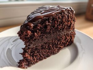 Close-up of a rich, dark slice of chocolate cake recipe topped with glossy chocolate ganache.