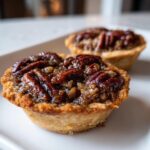 Close-up of two freshly baked mini pecan pies with glossy, caramelized pecan topping on a white plate.