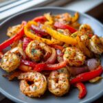 Close-up of perfectly seasoned shrimp fajitas mixed with sliced red and yellow bell peppers and onions on a gray plate.