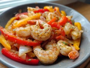 Close-up of perfectly cooked shrimp fajitas featuring seasoned shrimp, red and yellow bell peppers, and onions in a dark bowl.
