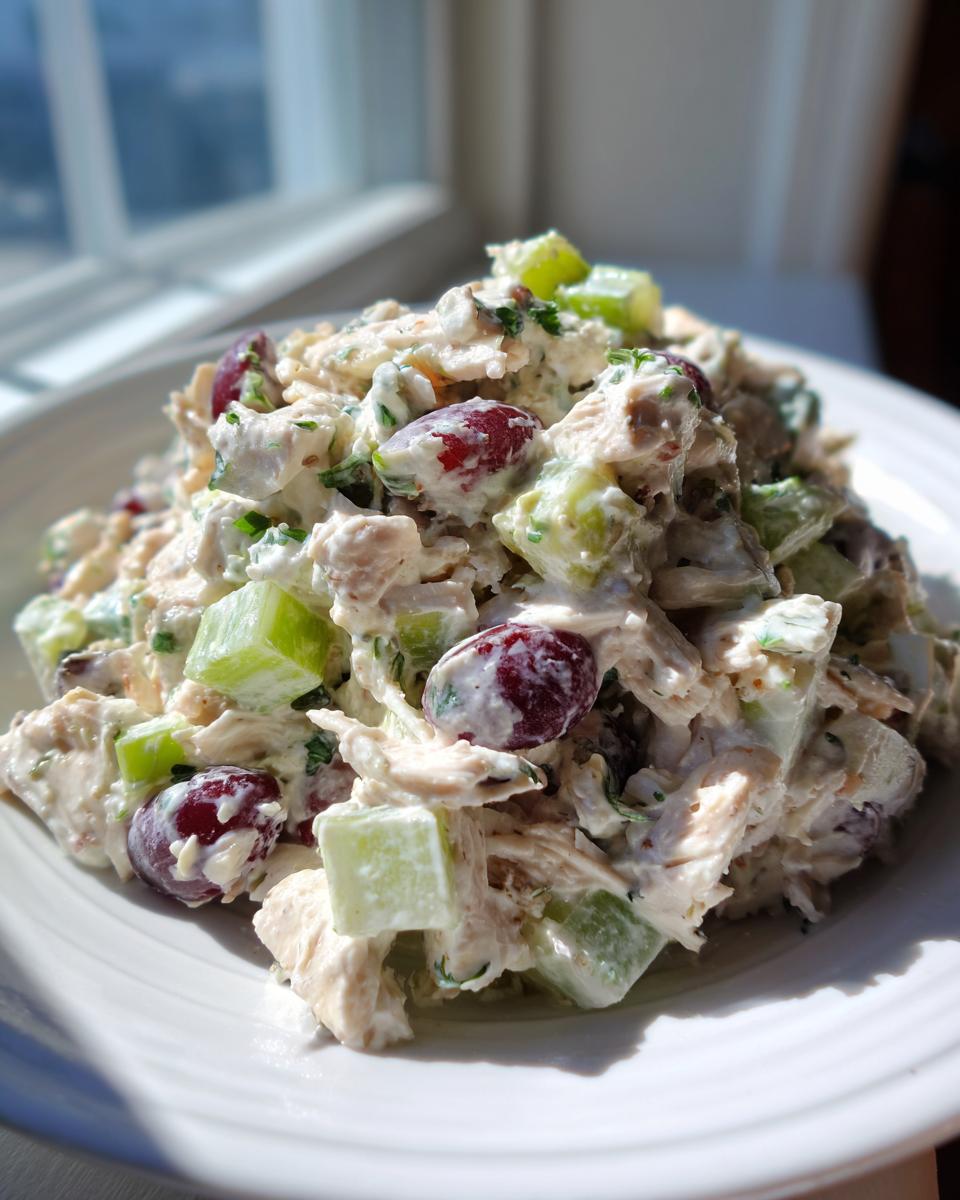 Close-up of creamy greek yogurt chicken salad mixed with red grapes and celery chunks on a white plate.