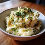 A bowl of creamy roasted garlic mashed potatoes topped with melted butter and fresh chopped chives.
