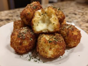 A stack of golden brown, crispy potato croquettes, one cut open showing a gooey melted cheese center.