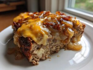 A close-up slice of crockpot french onion meatloaf topped with melted cheddar cheese and caramelized onions on a white plate.