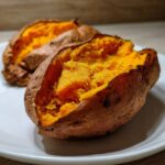 Close-up of two perfectly baked sweet potatoes split open showing the fluffy, bright orange interior.