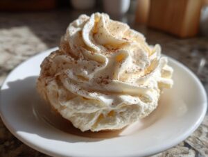 A dollop of fluffy, whipped cinnamon butter, dusted with spice, served on a small white plate.