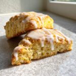 Close-up of two fluffy lemon scones stacked, drizzled generously with white lemon glaze.