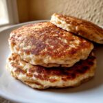 A close-up stack of three fluffy oatmeal pancakes with golden-brown, perfectly cooked surfaces.