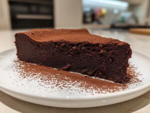 A rich, dark slice of flourless chocolate torte dusted heavily with cocoa powder on a white plate.