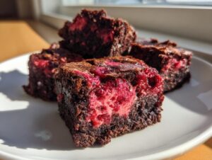 Close-up of fudgy strawberry brownies with a bright pink, fruity center on a white plate.