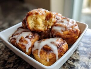 Close-up of several fluffy cinnamon roll bites drizzled with white icing, one is broken open showing the soft interior.