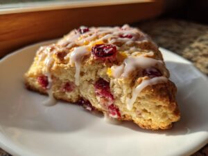A close-up of a freshly baked cranberry scones wedge drizzled with white vanilla glaze, sitting on a white plate.