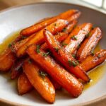 Close-up of perfectly glazed roasted carrots glistening in a sauce, garnished with fresh thyme.