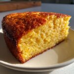 A close-up of a moist, golden slice of skillet cornbread with a beautifully browned, slightly glazed crust.