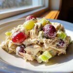 A serving of creamy greek yogurt chicken salad mixed with celery and topped with red and green grapes.