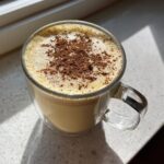 A glass mug filled with creamy homemade eggnog, topped with foam and a dusting of cinnamon.