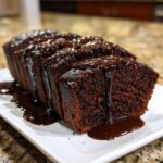A loaf of rich, dark chocolate hot fudge brownie bread sliced and generously covered with dripping hot fudge sauce.