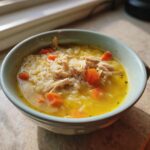 Close-up of a light blue bowl filled with Lemon Ginger Turmeric Chicken and Rice Soup, showing shredded chicken, white rice, and bright orange carrots.