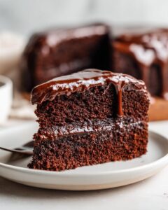 Close-up of a rich slice of moist chocolate cake layered with filling and topped with dripping chocolate ganache.