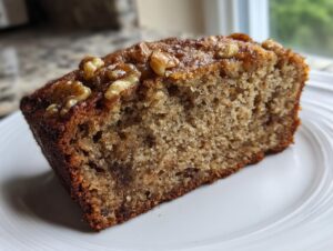 Close-up of a moist slice of banana bread recipe topped with glazed walnuts on a white plate.