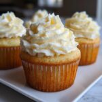 A close-up of a perfectly baked vanilla cupcake topped with a generous swirl of white vanilla frosting.