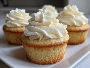 Close-up of moist vanilla cupcakes topped with high swirls of white buttercream frosting.