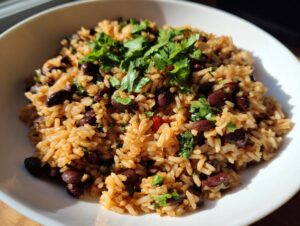 A close-up of a white bowl filled with seasoned rice and black beans and rice, topped with fresh cilantro.