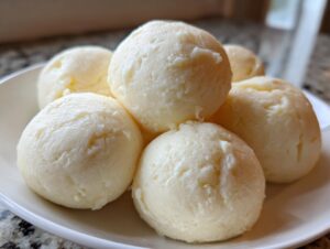 A close-up of several smooth, pale yellow balls of freshly made fufu dough served on a white plate.