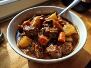 Close-up of a rich, dark bowl of 8 hour pork stew featuring tender meat chunks, potatoes, and carrots.