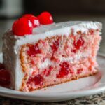 Close-up of a moist slice of pink cherry cake layered with white frosting and topped with maraschino cherries.