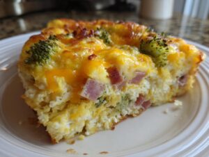 Close-up of a hearty slice of egg bake with melted cheddar cheese, ham cubes, and broccoli florets.