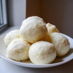 A pile of smooth, white balls of fufu dough served on a white plate, ready to eat.