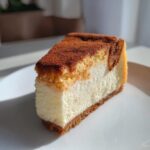 A thick, creamy slice of snickerdoodle cheesecake topped with cinnamon sugar, served on a white plate.