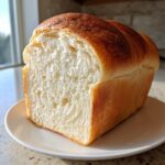 A close-up of a freshly baked sourdough sandwich bread loaf, showing a soft, white, even crumb structure.