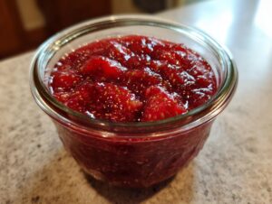 Close-up of bright red strawberry freezer jam packed with whole fruit pieces in a clear glass jar.