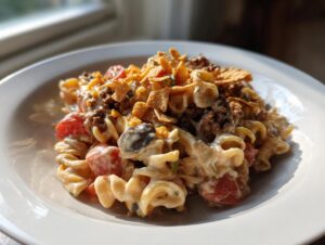 A close-up of a creamy taco pasta salad featuring rotini pasta, ground meat, tomatoes, and crushed tortilla chips.