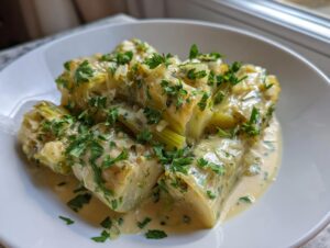 Close-up of tender braised leeks segments smothered in a creamy sauce and topped with fresh parsley.